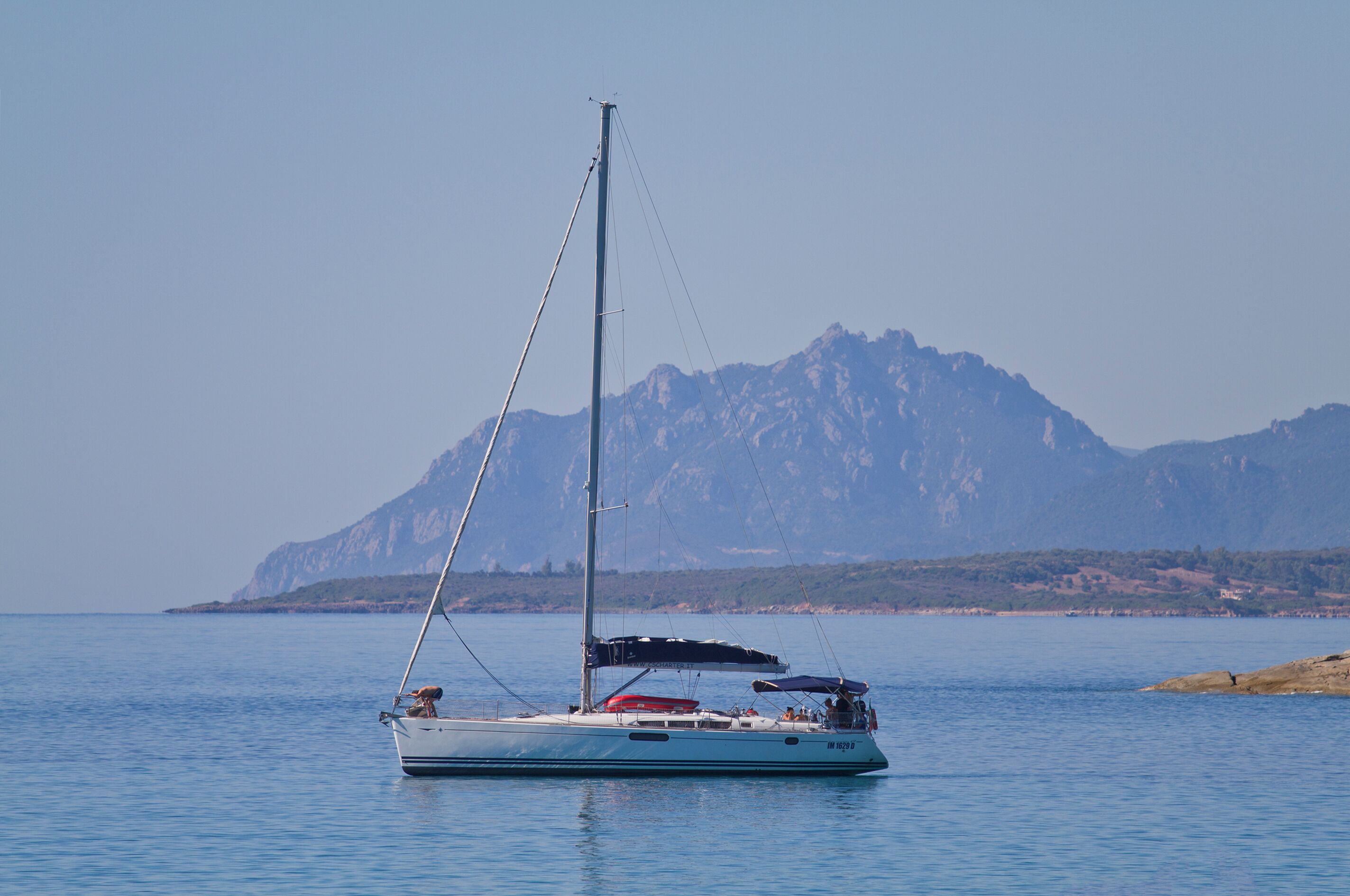 A sailboat on calm waters with a mountain range in the background.
