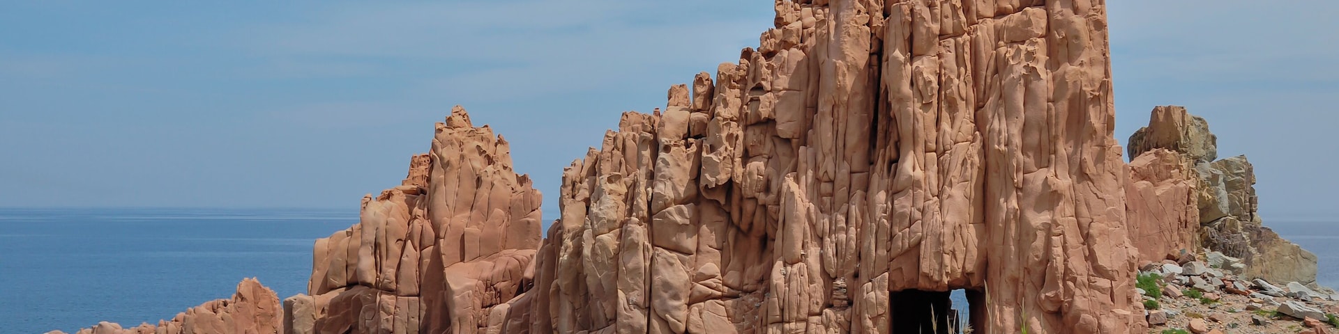Un paisaje costero rocoso con una formación rocosa destacada y la entrada de una cueva.