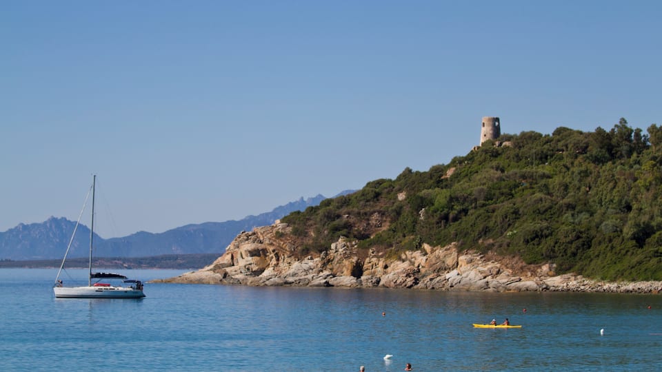 A sailboat on calm waters, a yellow kayak, and a castle on a hill.