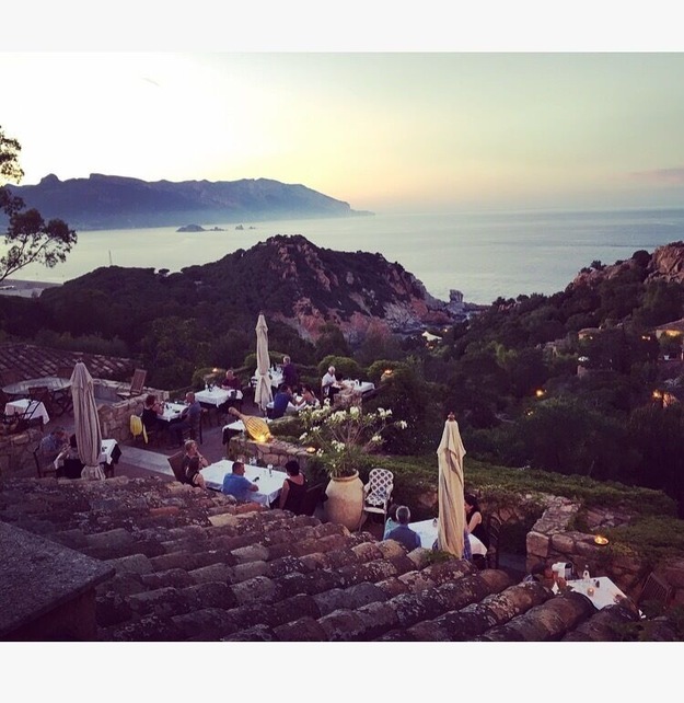 Ein Küstenrestaurant mit Terrassensitzplätzen mit Blick auf das Meer, umgeben von felsigem Gelände und Vegetation.