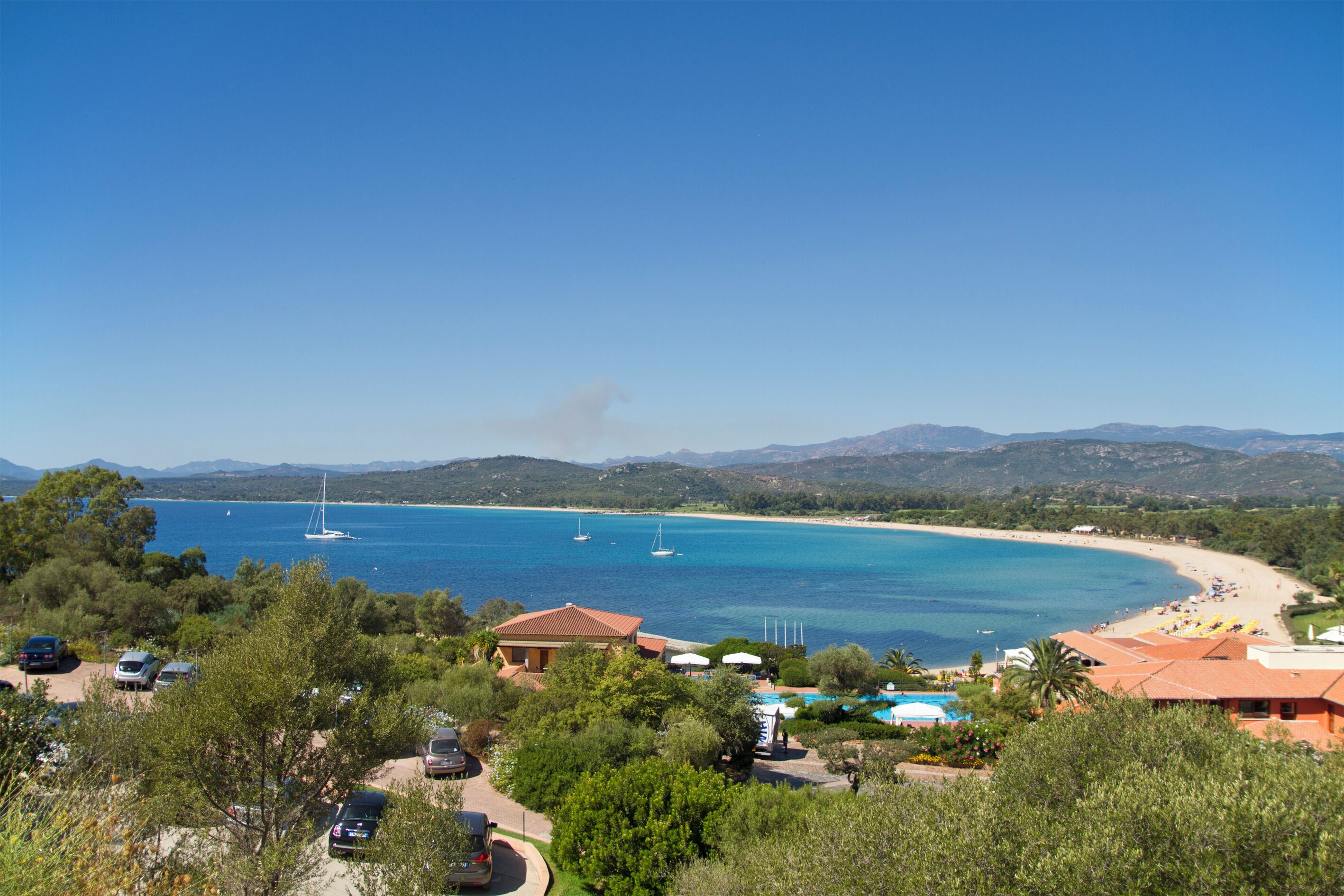 A coastal area with a beach, sailboats, and a clear blue sky.