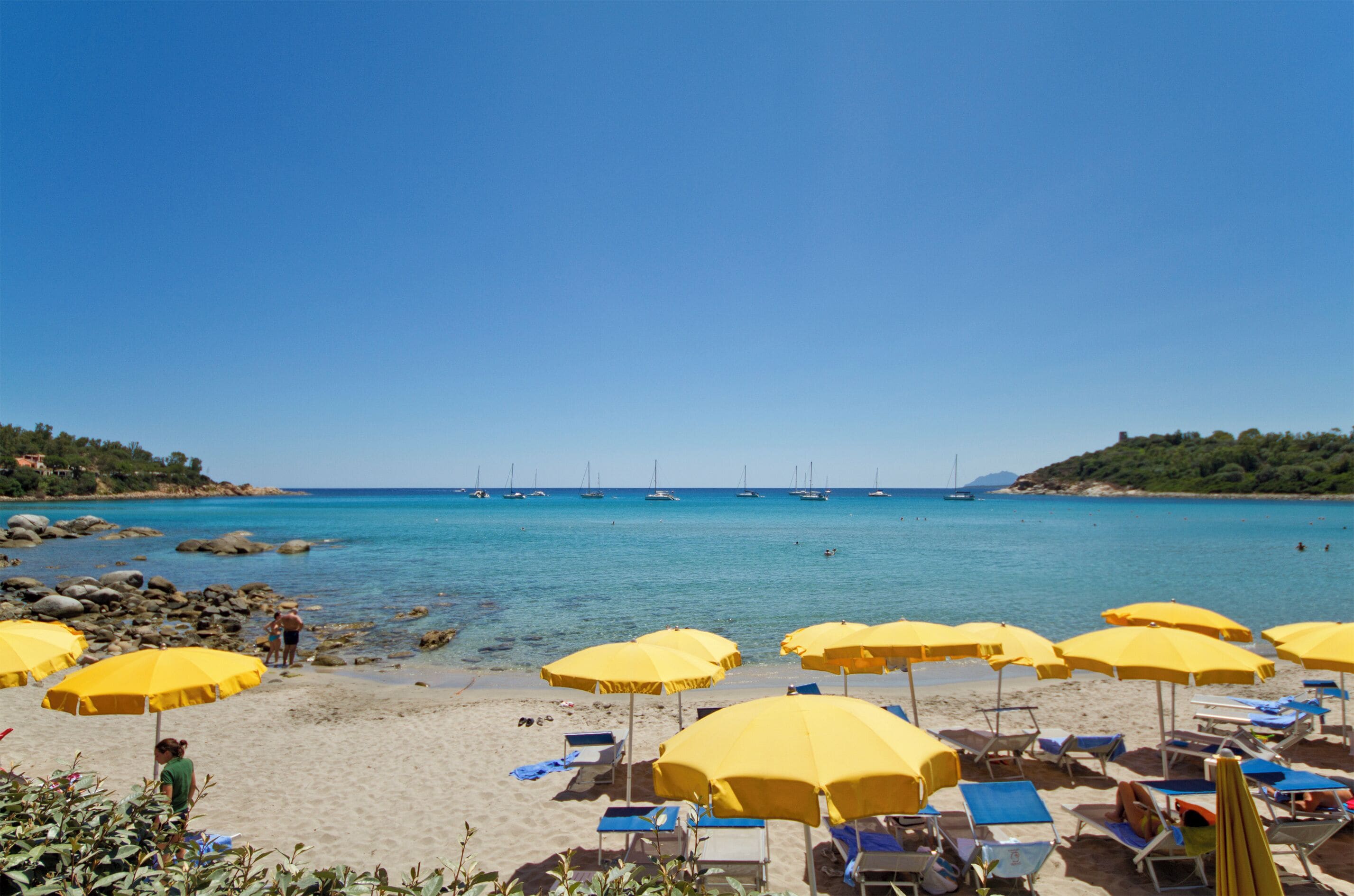 A beach with yellow umbrellas and blue lounge chairs.