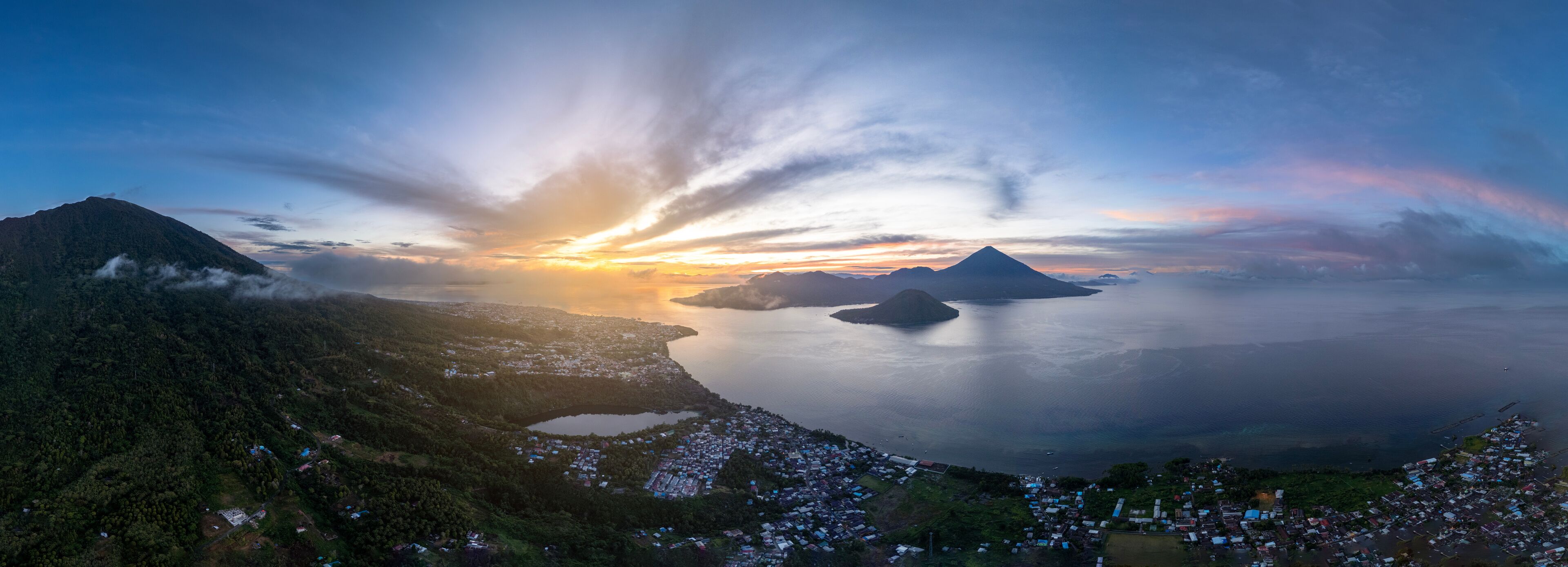 A panoramic view of a coastal landscape with mountains, a body of water, and a village.