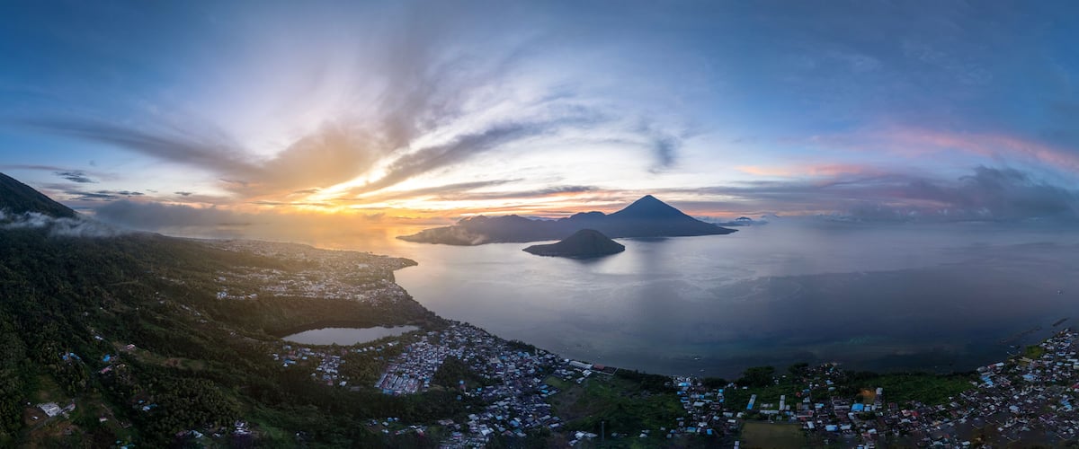 A panoramic view of a coastal landscape with mountains, a body of water, and a village.
