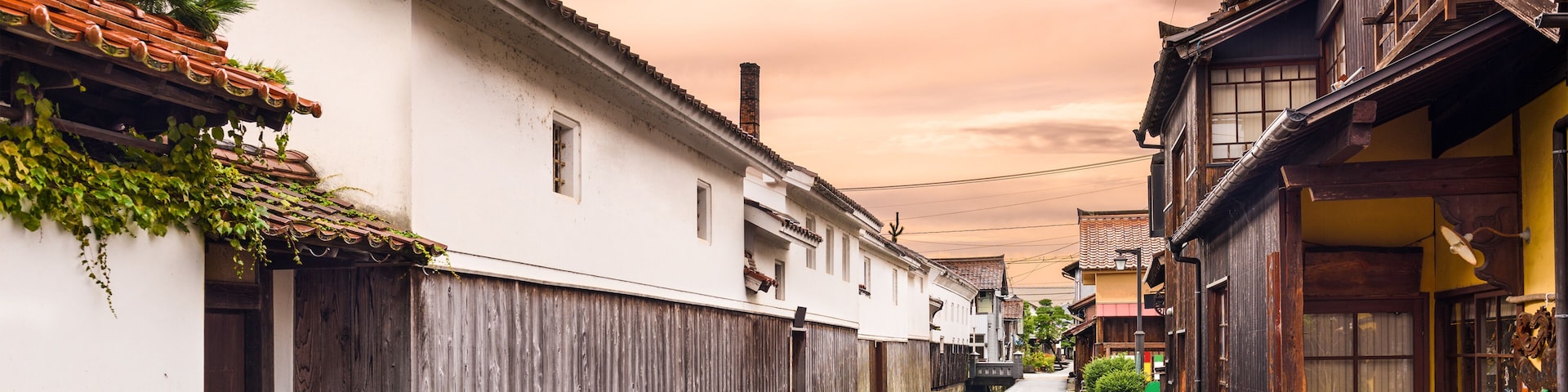 Uma rua estreita com casas tradicionais de madeira, um canal de água de pedra e um céu nublado.