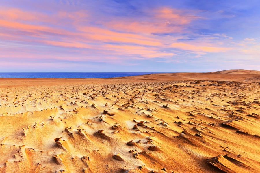 Weite Wüstenlandschaft mit wellenförmigen Sanddünen unter einem farbenprächtigen Himmel.