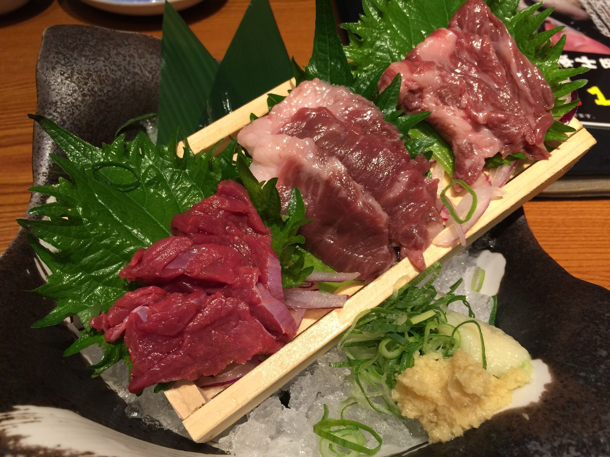 A variety of raw fish on a wooden skewer, garnished with green leaves and thinly sliced onions, served on a bed of ice.
