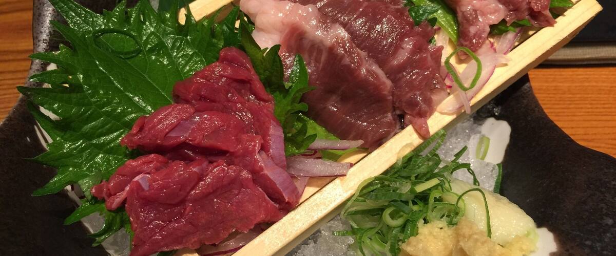 A variety of raw fish on a wooden skewer, garnished with green leaves and thinly sliced onions, served on a bed of ice.