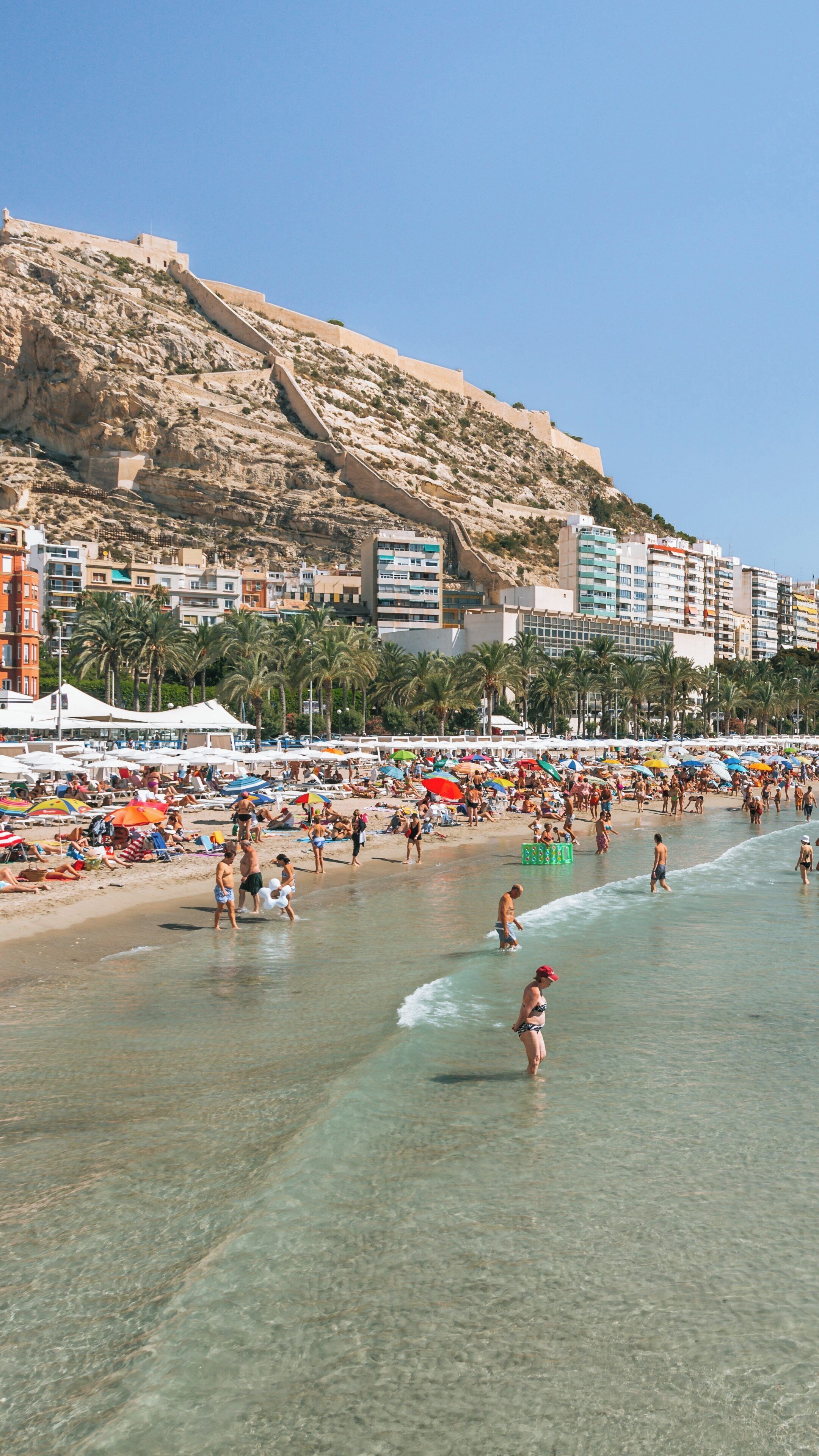 Vibrant summer day at Postiguet Beach in Alicante, Valencian Community, Spain, featuring sunbathers and clear blue waters