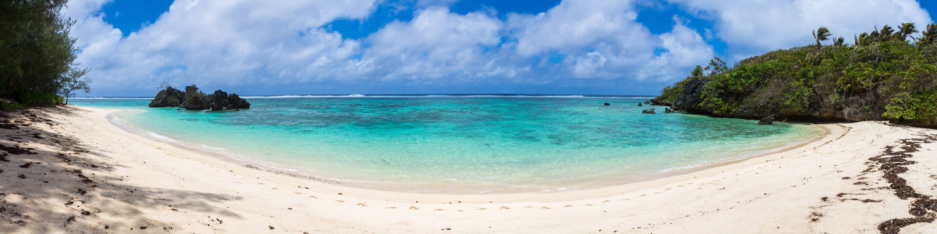 A beach with clear turquoise water, white sand, and scattered rocks.