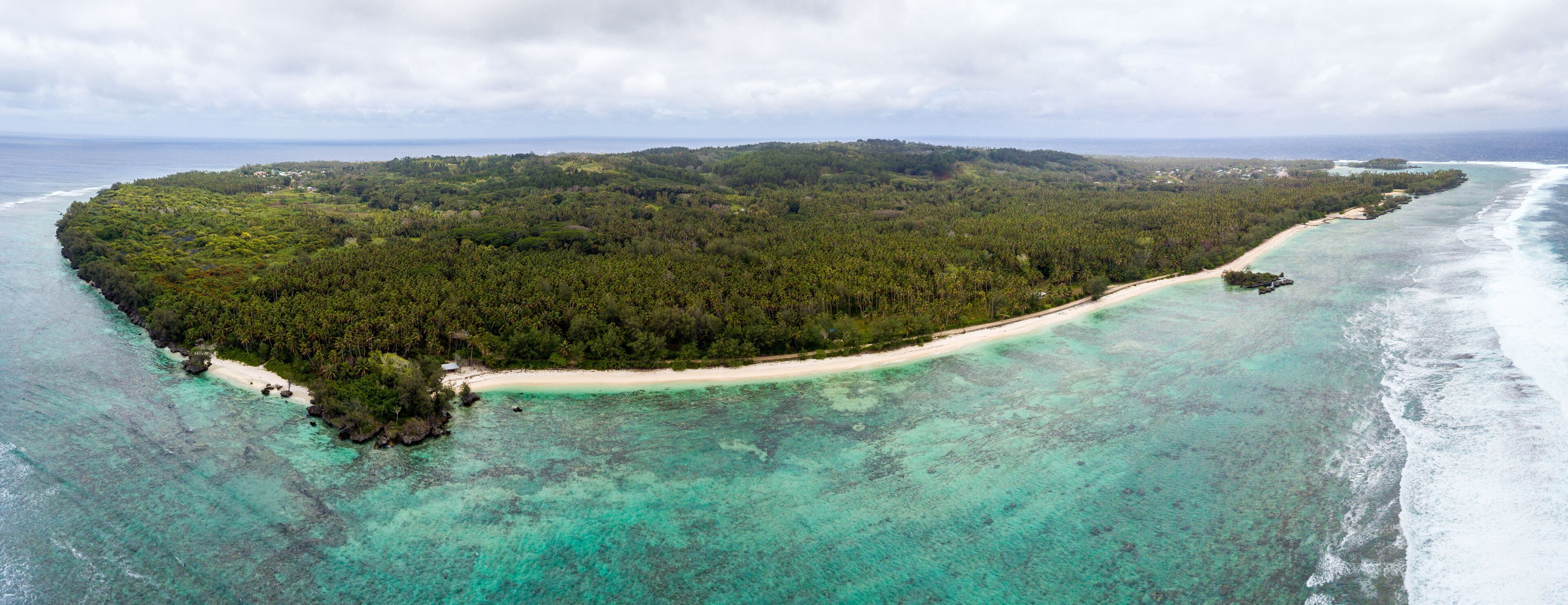 An aerial view of a tropical island with a sandy beach, clear turquoise waters, and dense green forest.