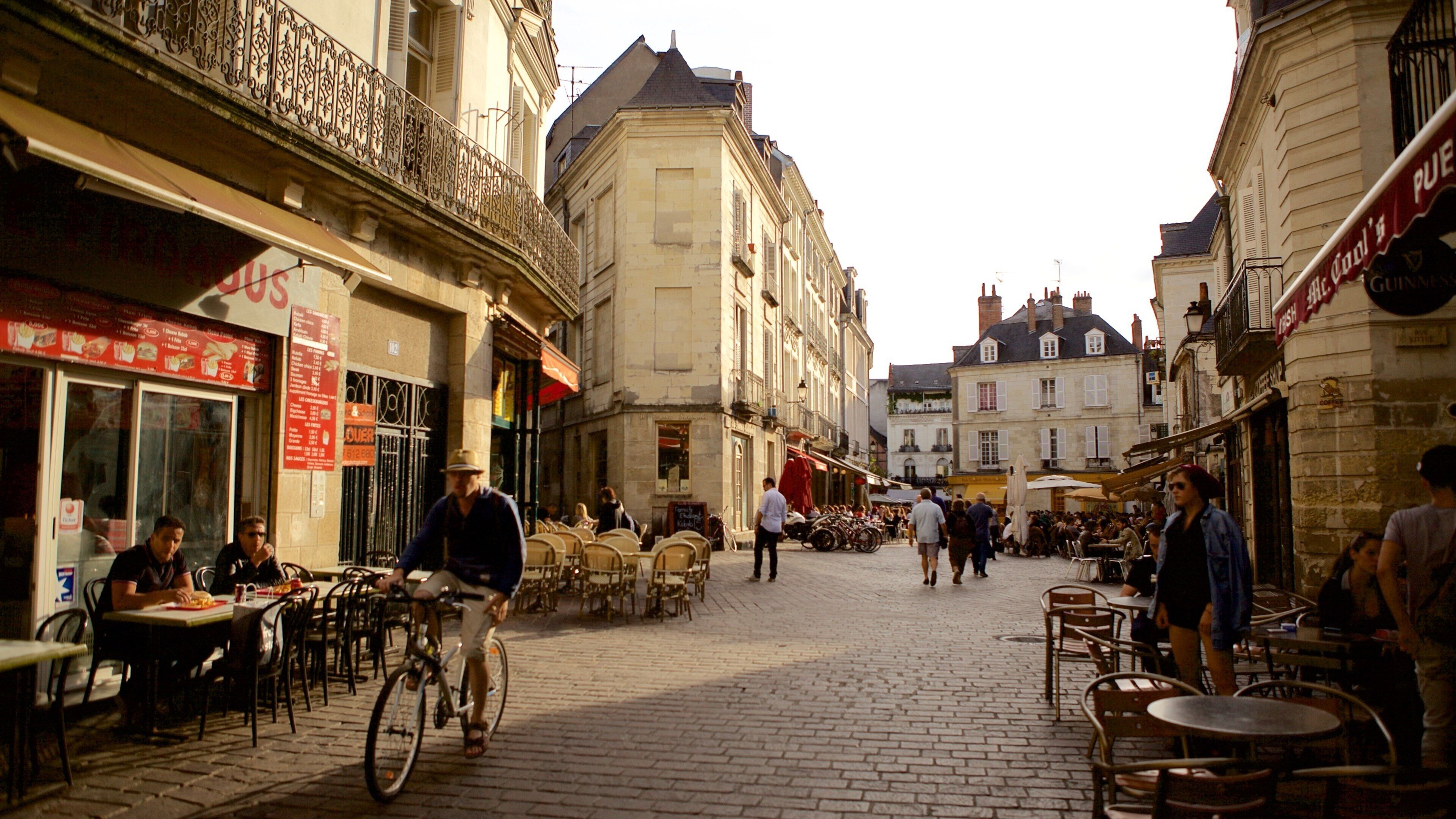 A cobblestone street with outdoor cafes, bicycles, and pedestrians.