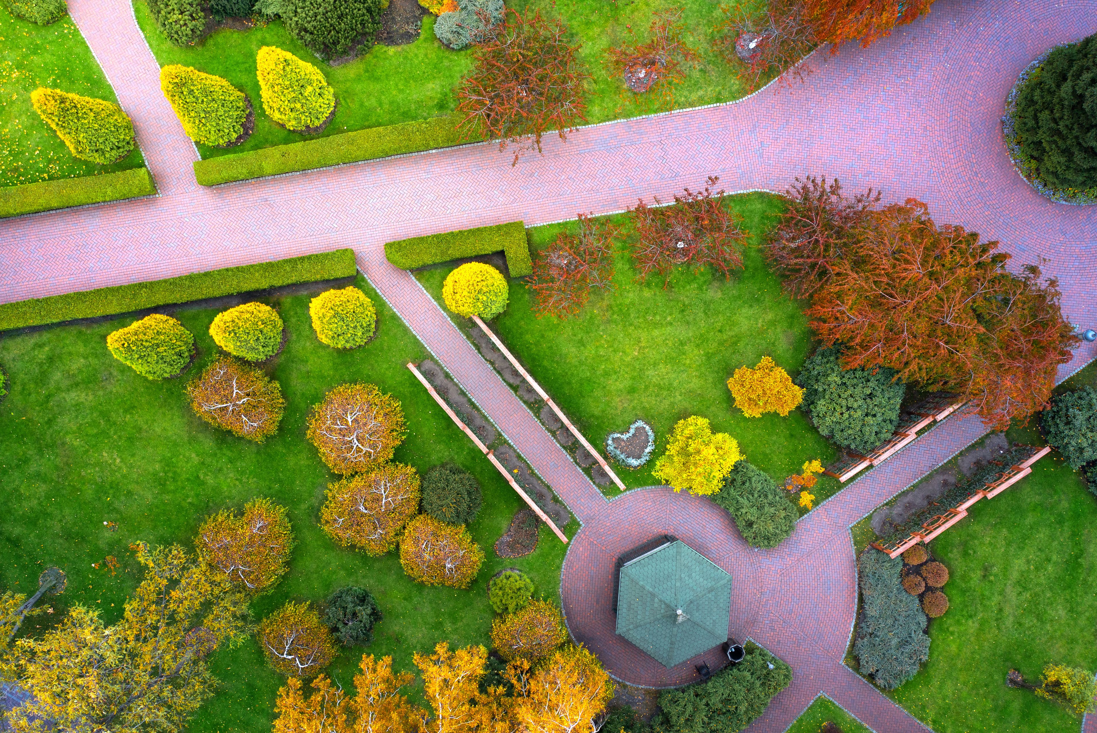 Jardim ajardinado com caminhos, sebes bem aparadas e uma área circular central com um gazebo.