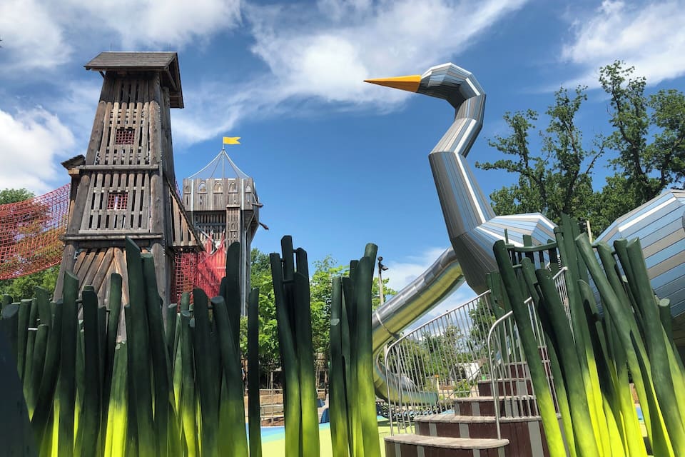 A wooden tower, a large bird sculpture, and a slide in a park.