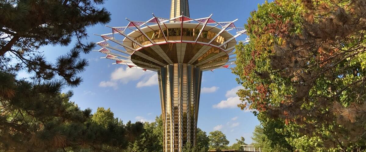 A tall tower with a spire, surrounded by trees.