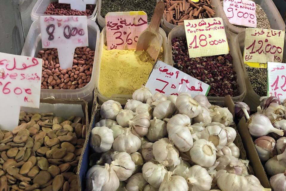 A market stall with various food items like garlic, chickpeas, and spices, each with price tags.
