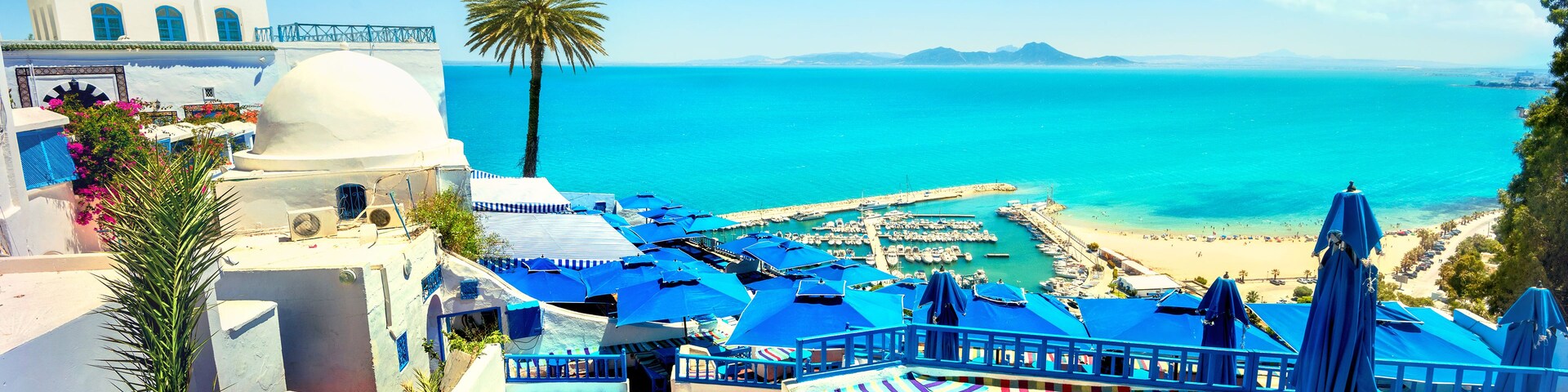 Un complejo turístico frente al mar con sombrillas azules, sillas de descanso a rayas y vistas al océano.