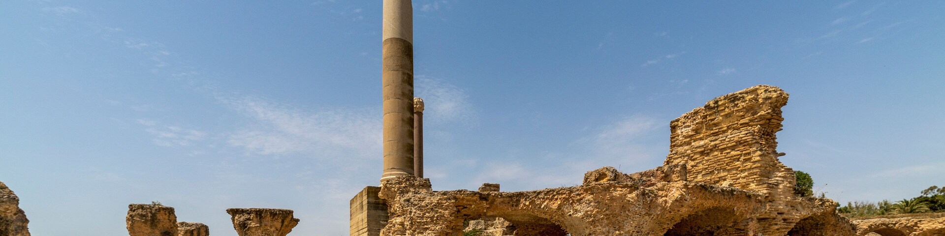 Ruínas antigas com uma coluna alta e arcos de pedra.