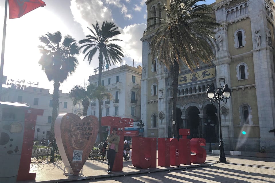 A historic building with ornate architecture, palm trees, and a large heart-shaped sculpture.