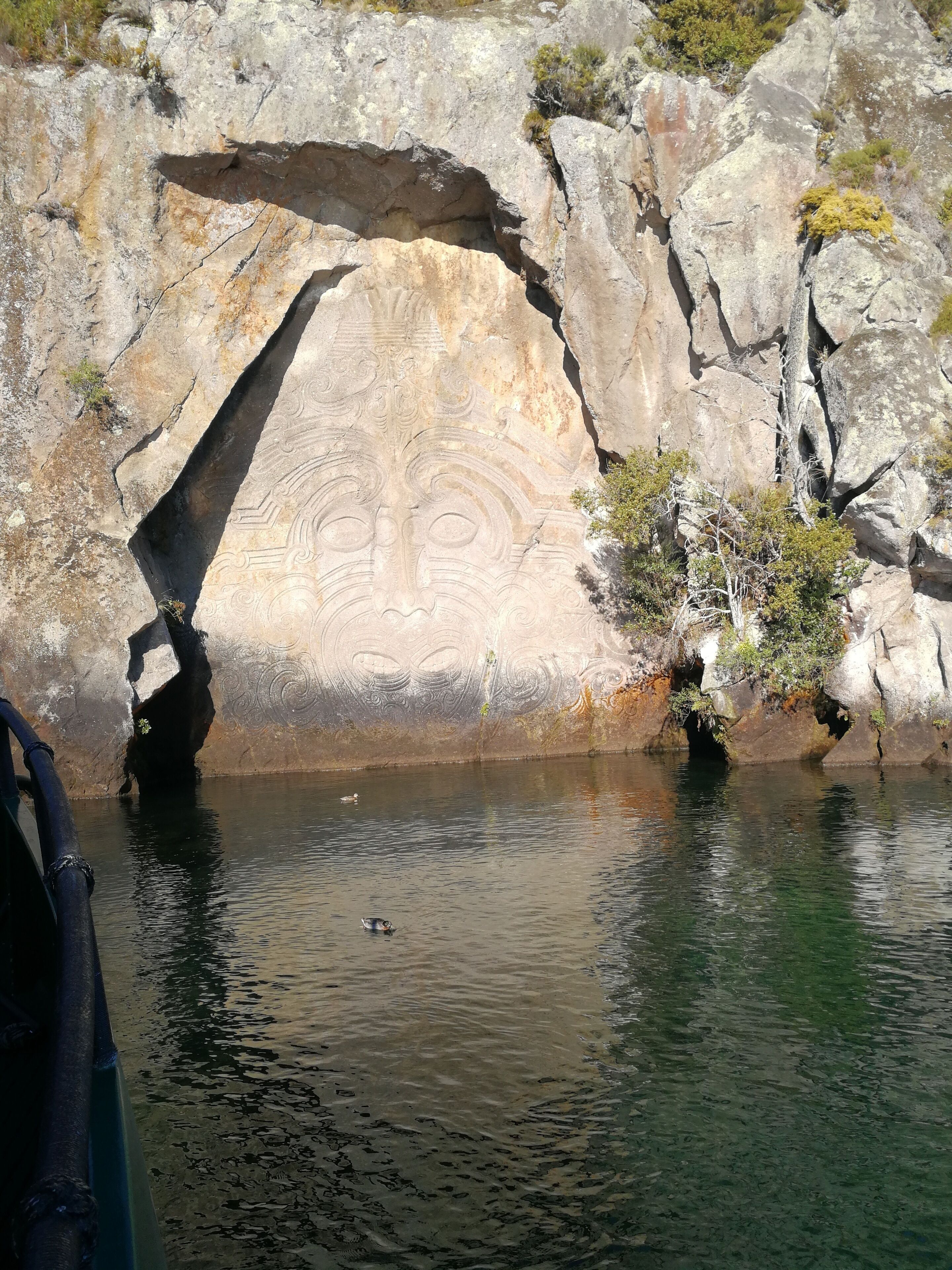 A rock formation with carvings, a body of water, and some vegetation.