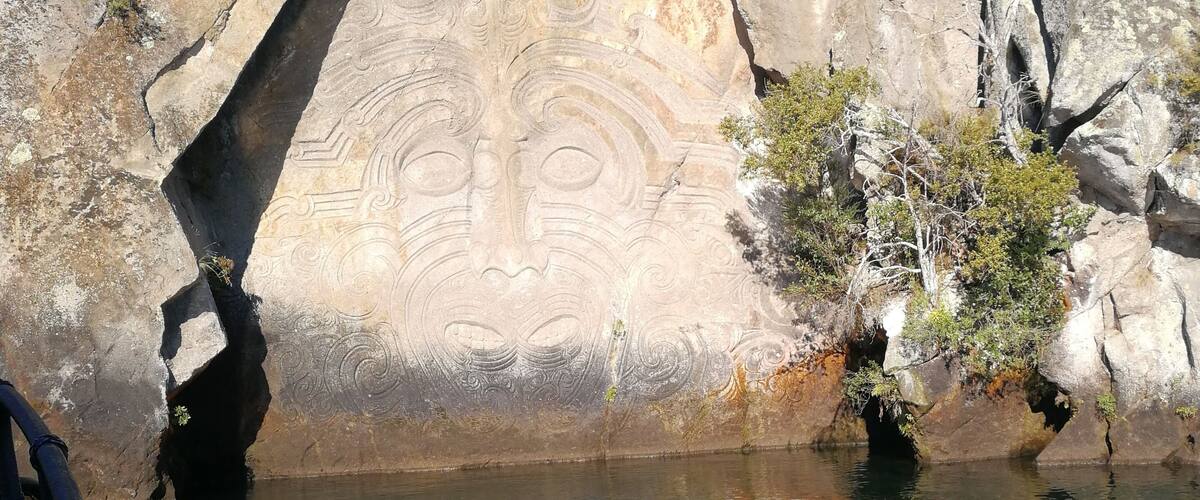 A rock formation with carvings, a body of water, and some vegetation.