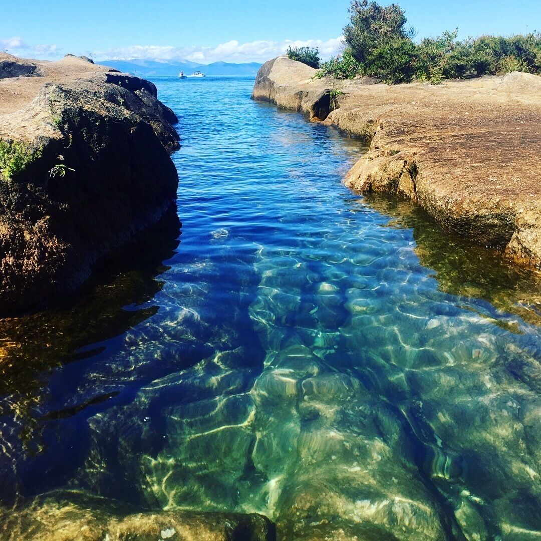 A clear blue stream surrounded by rocky terrain and distant mountains.