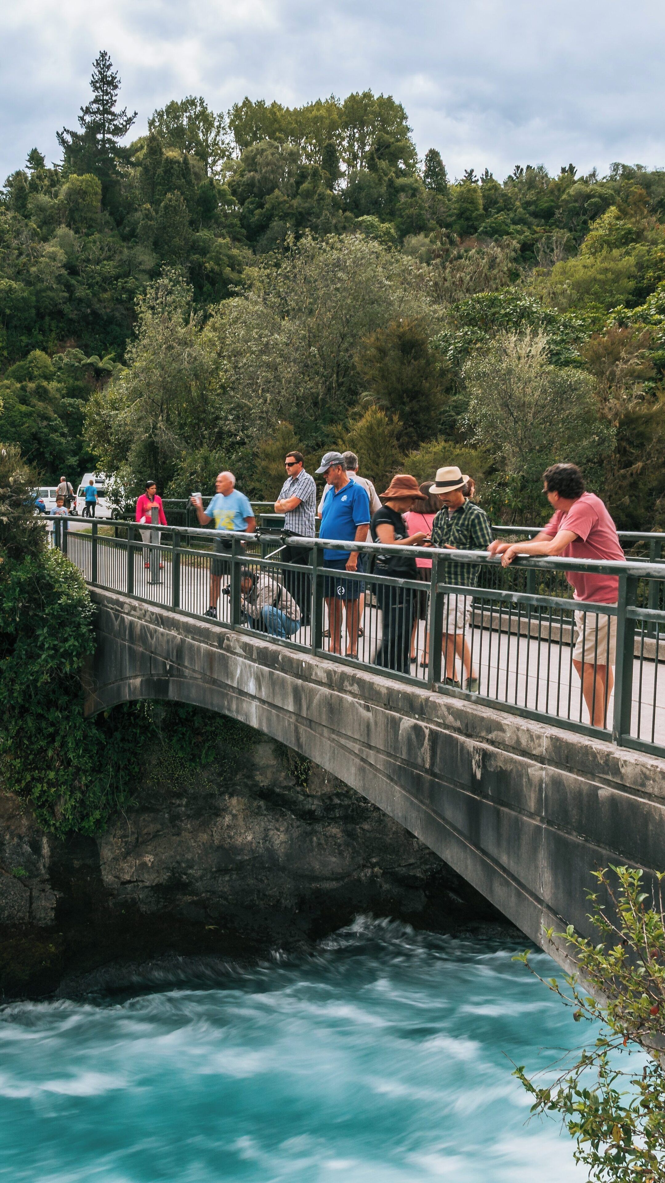 Visitors enjoying breathtaking views at Huka Falls in Taupo, New Zealand on a serene day amidst lush greenery and flowing waters