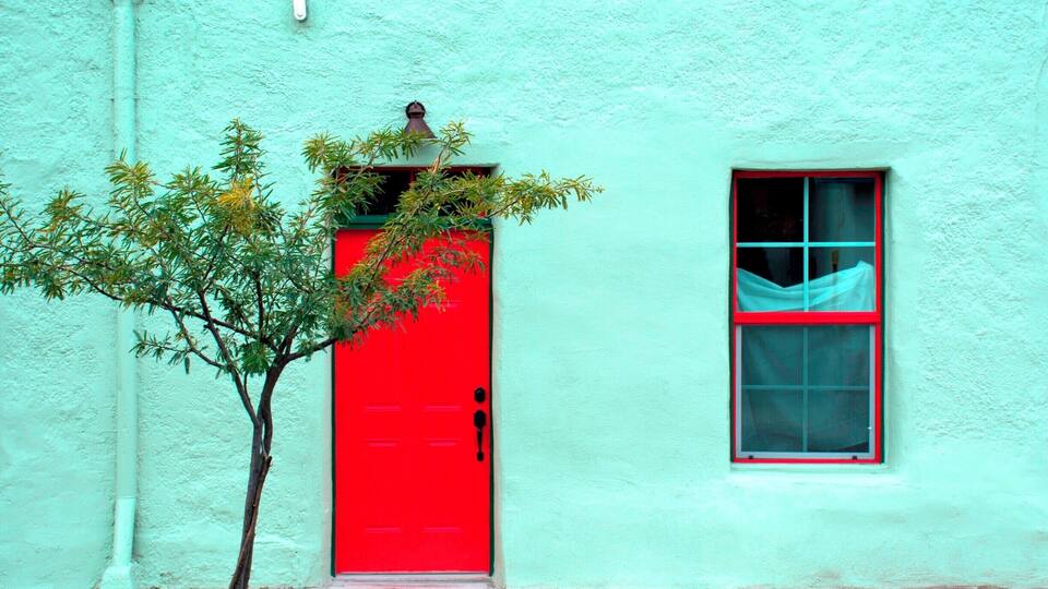 A turquoise building with a red door and a window with a blue curtain.