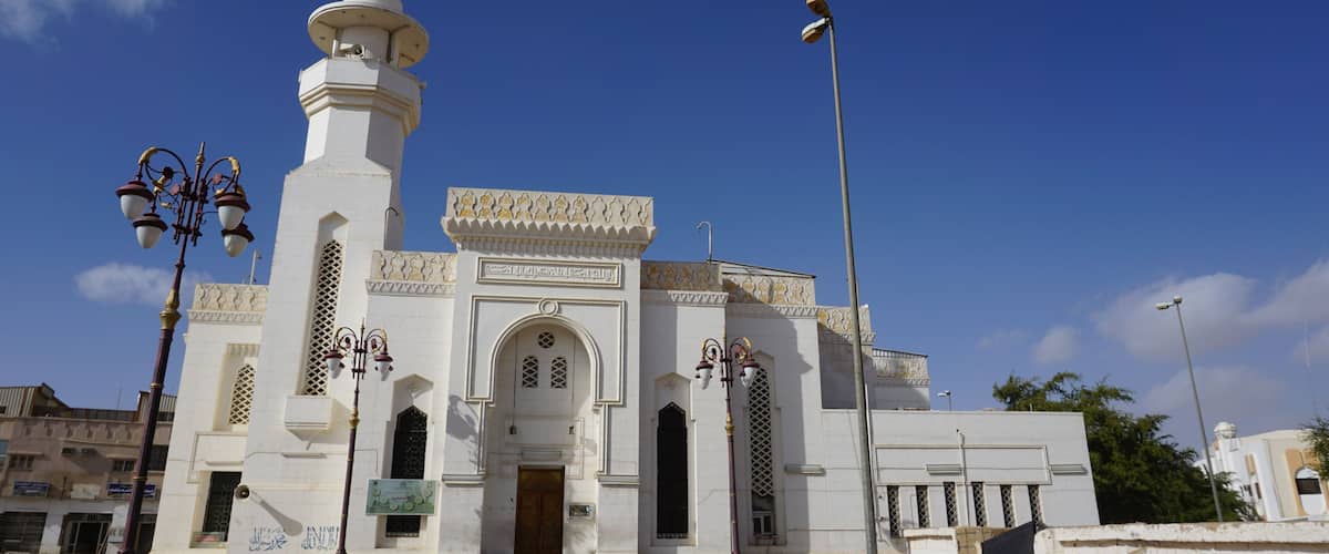 A white mosque with a minaret, arched windows, and a wooden door.