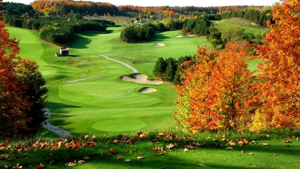 A golf course with autumn foliage, sand bunkers, and a clubhouse.