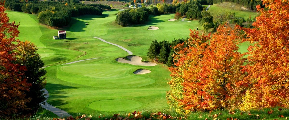 A golf course with autumn foliage, sand bunkers, and a clubhouse.