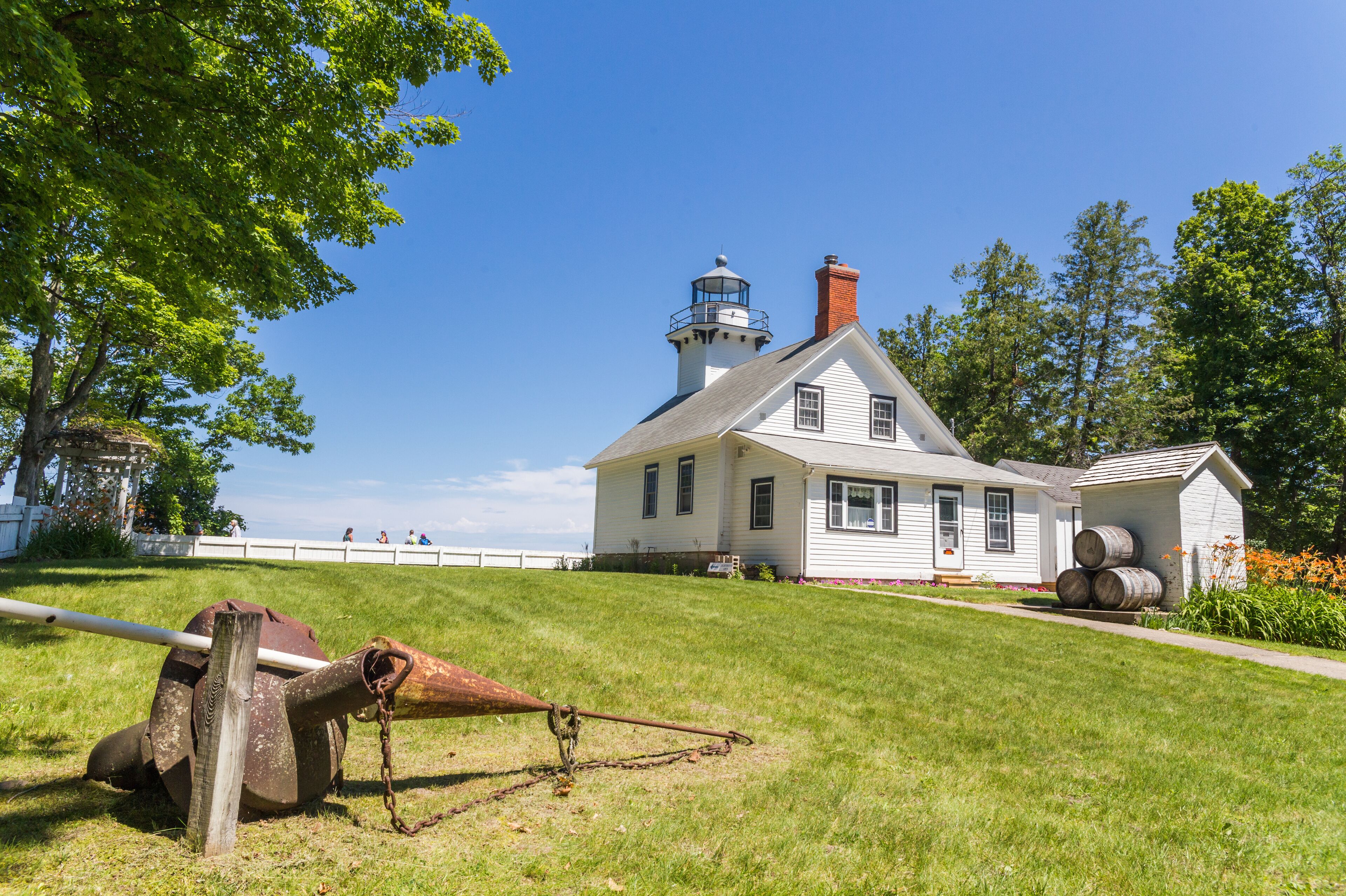A white lighthouse with a red roof, a grassy hill, and a wooden barrel in the foreground.