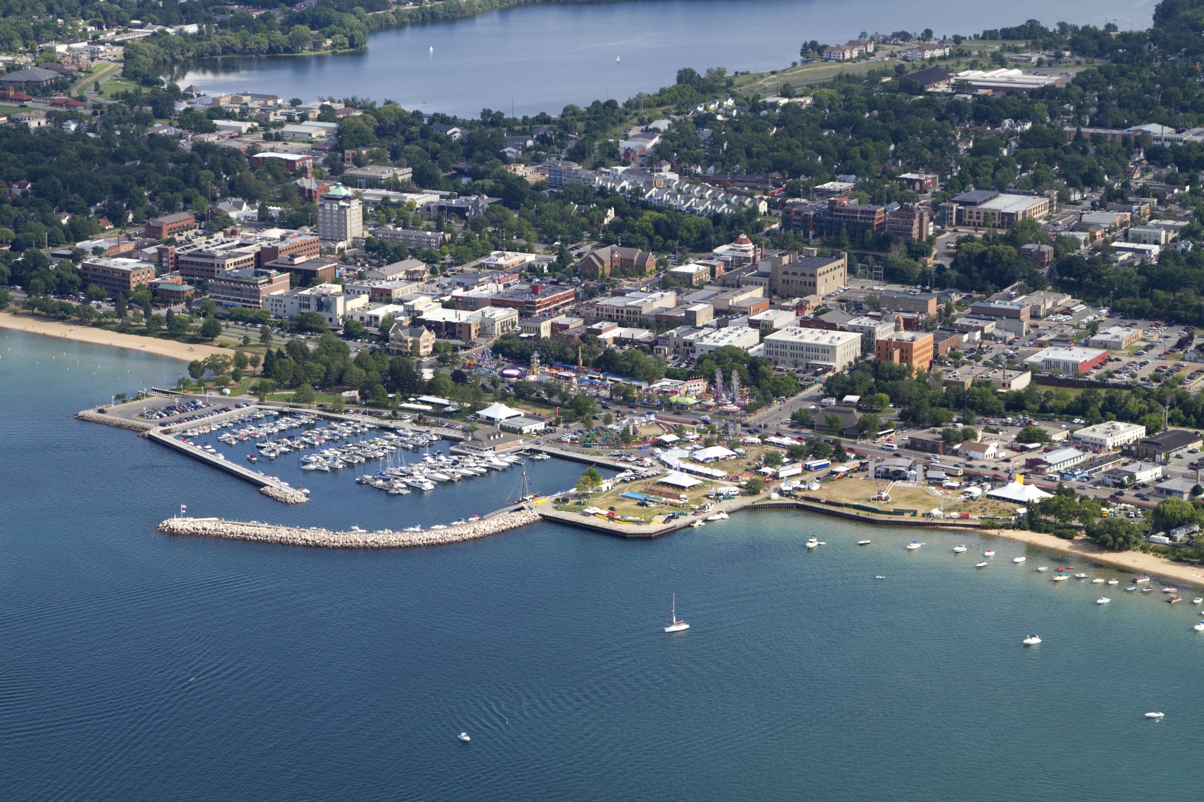 An aerial view of a coastal city with a marina, buildings, and a hilly landscape in the background.