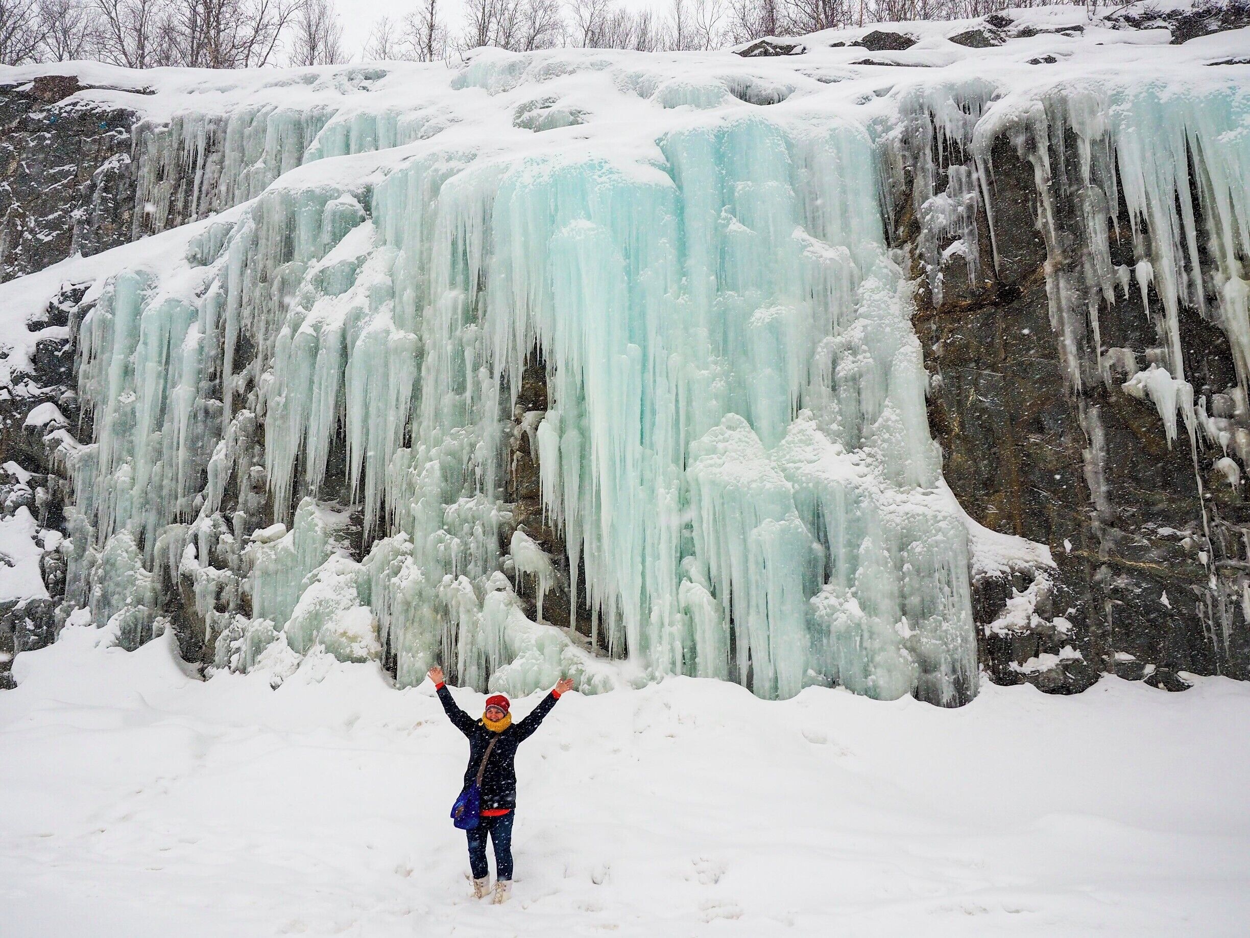 A person standing in front of a large ice waterfall.