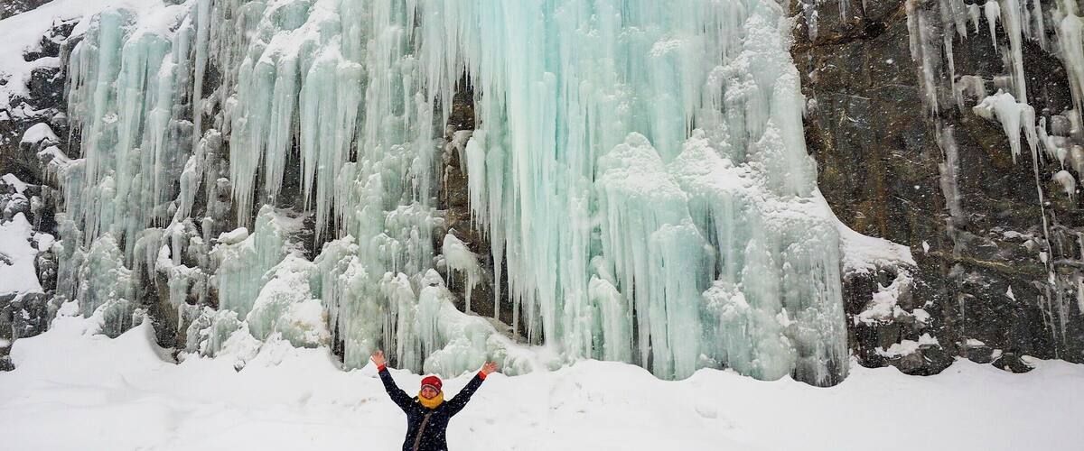 A person standing in front of a large ice waterfall.