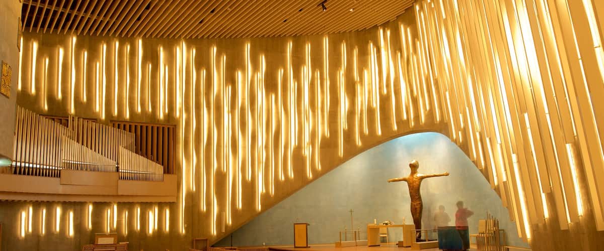 Een kerkinterieur met een houten orgel, rijen stoelen en een kruis.