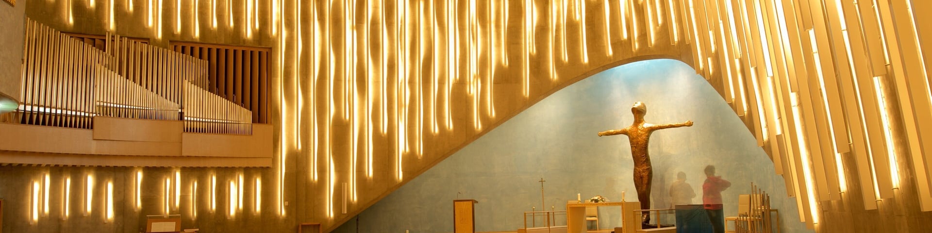 Interior de iglesia con un órgano de madera, hileras de sillas y una cruz.