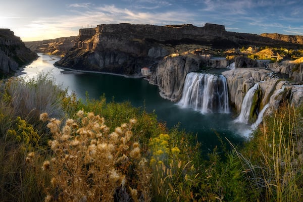 A waterfall cascading into a river surrounded by cliffs and vegetation.