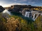 Une cascade se jetant dans une rivière, le tout entouré de falaises et de végétation.