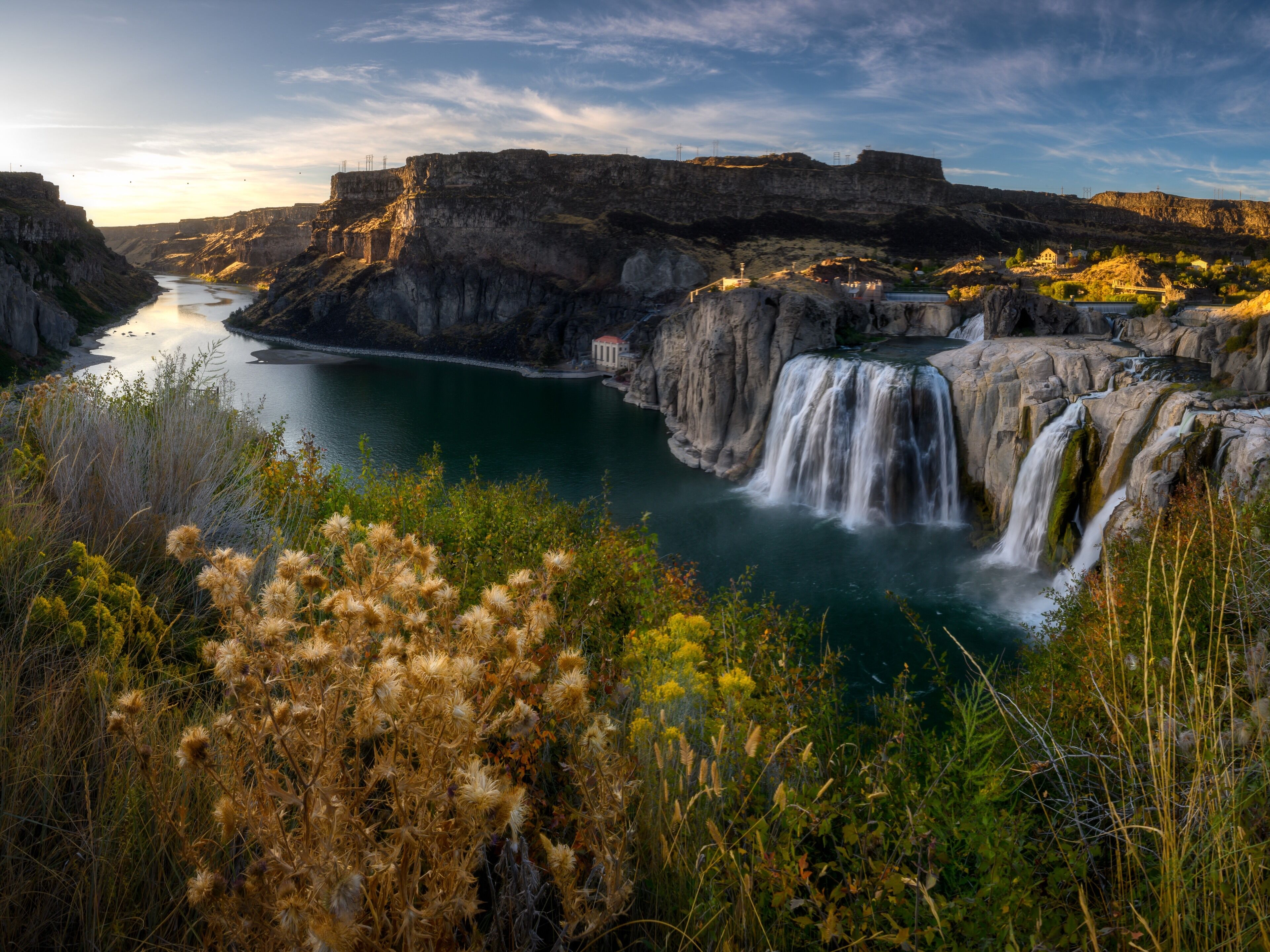 A waterfall cascading into a river surrounded by cliffs and vegetation.