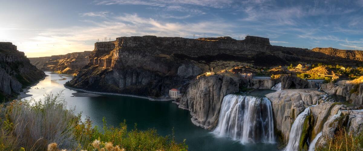 A waterfall cascading into a river surrounded by cliffs and vegetation.