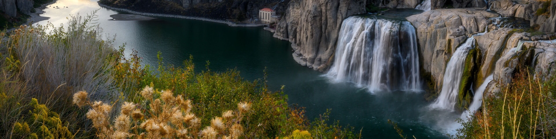 A waterfall cascading into a river surrounded by cliffs and vegetation.