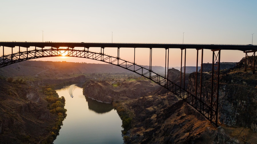 Un puente de acero arqueado sobre un río, con un atardecer de fondo.