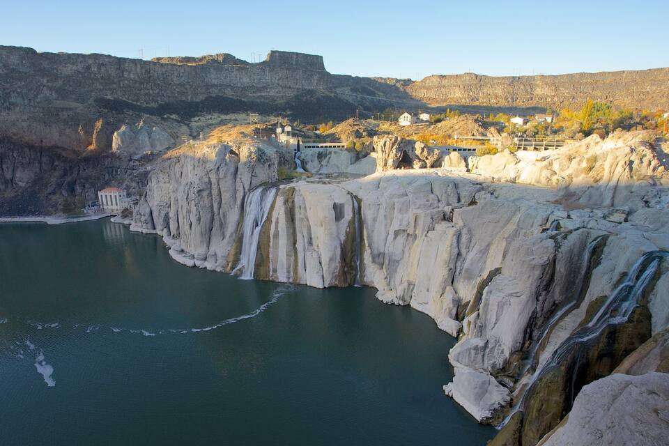 Una cascada que aboca a un llac envoltat de penya-segats rocosos i un petit assentament.