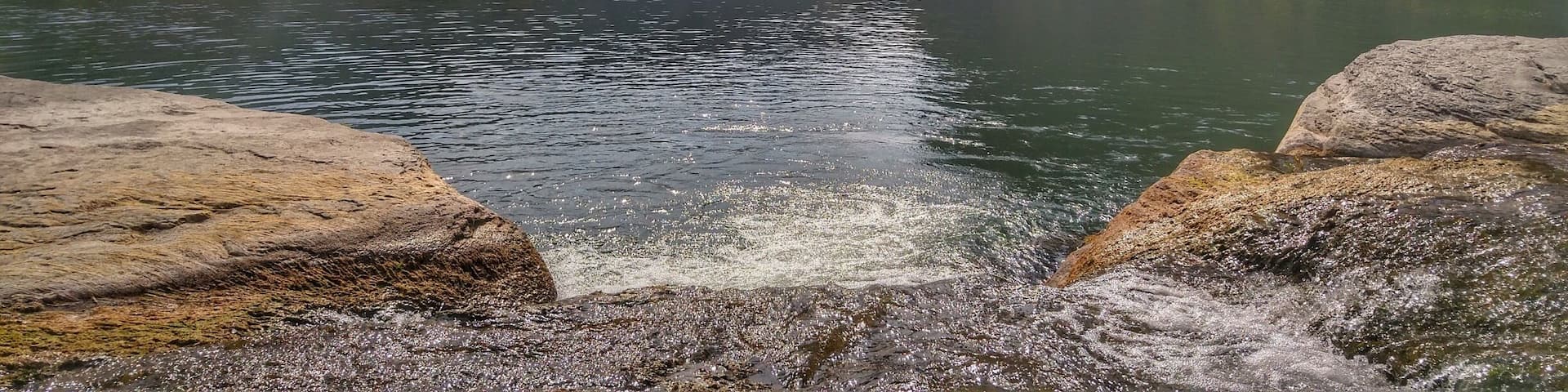 A calm river with rocky banks and steep cliffs in the background.