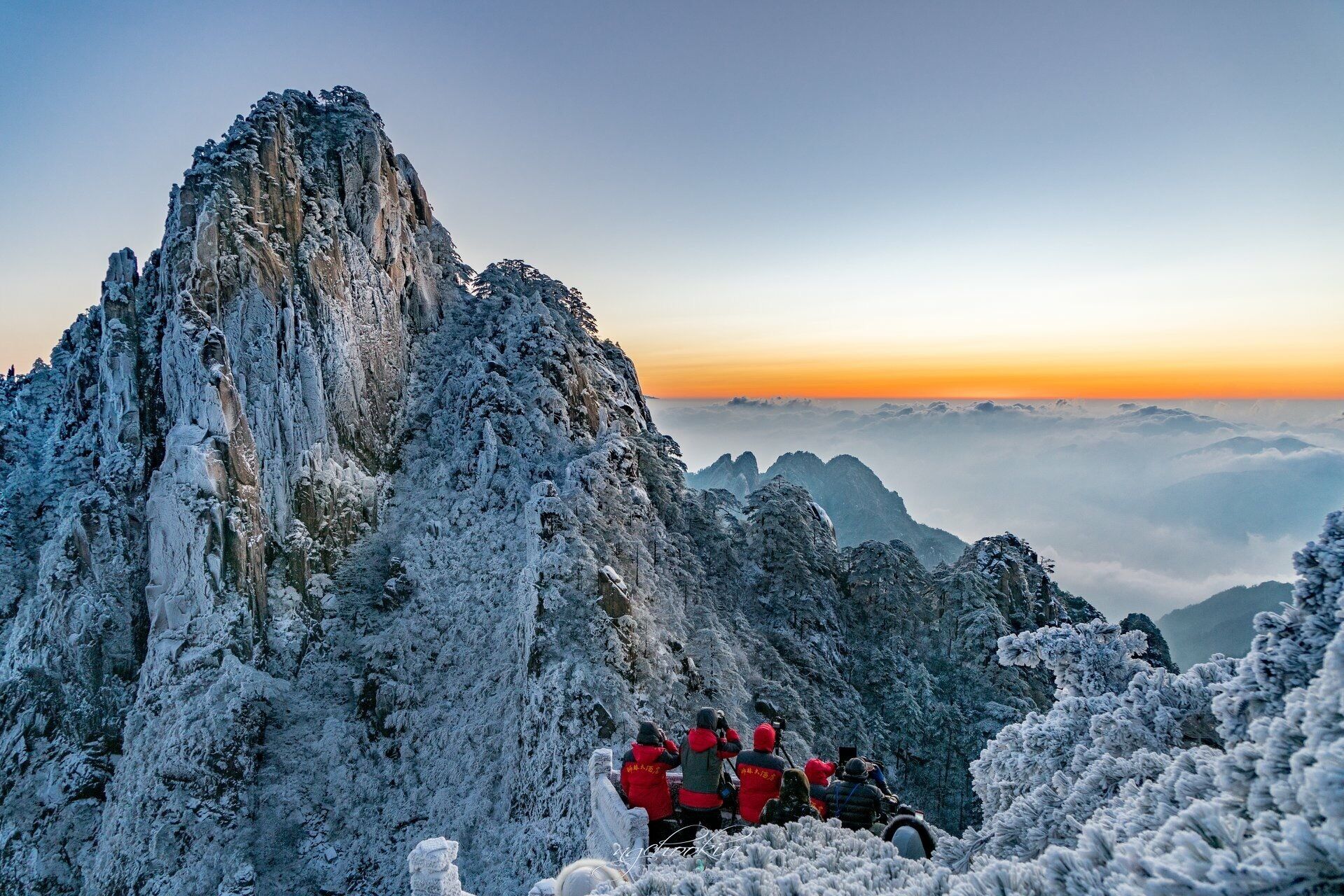 Un pico nevado de montaña con un grupo de personas con chaquetas rojas en la base.