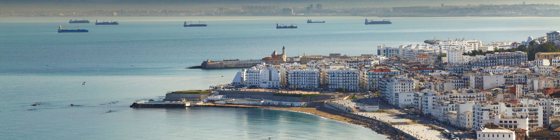 Uma cidade costeira com um porto, navios e um estádio.