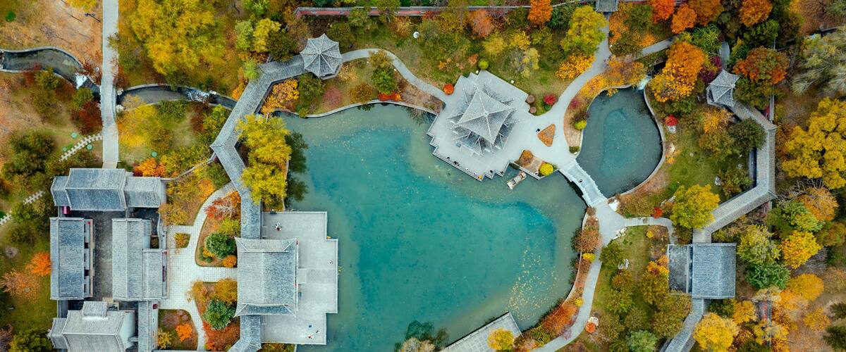 An aerial view of a park with a central pond, surrounding pathways, and traditional architecture.