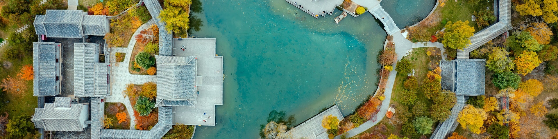 An aerial view of a park with a central pond, surrounding pathways, and traditional architecture.