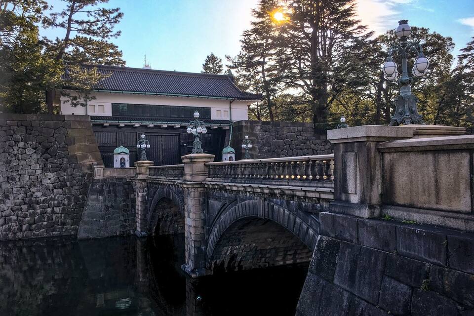 A stone bridge over a canal with a building and trees in the background.